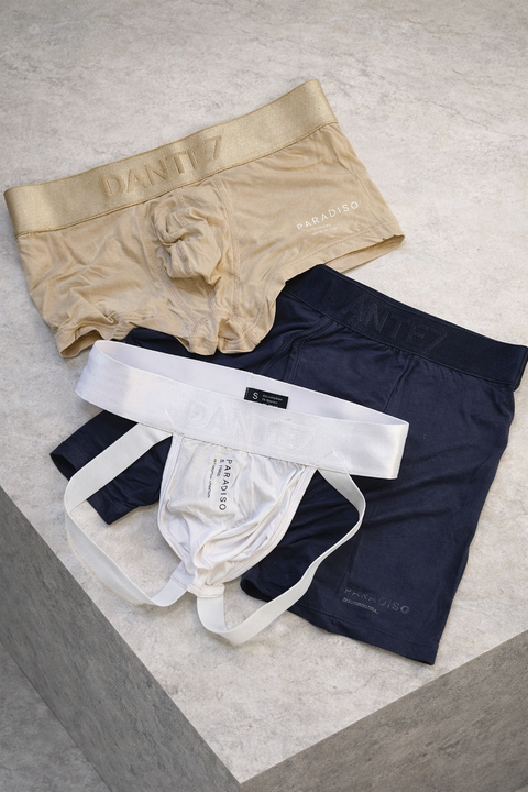 Three pairs of underwear in beige, navy, and white on a light gray surface.
